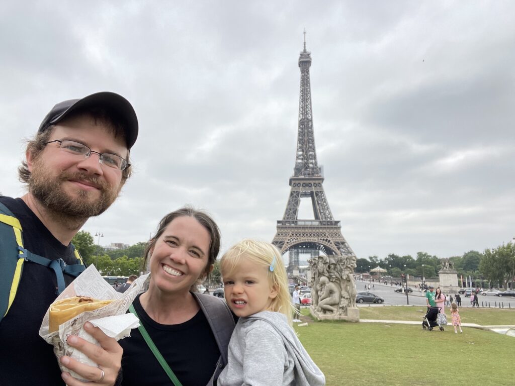 Parents and toddler eat a crepe in front of the eiffel tower